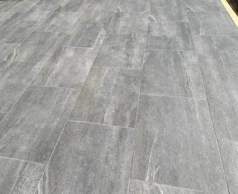 Close-up of a floor with large rectangular grey tiles that have subtle white marbled patterns and visible grout lines.